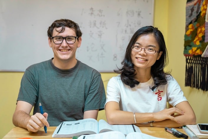 chinese teacher and student in class sitting at wooden table in front of whiteboard