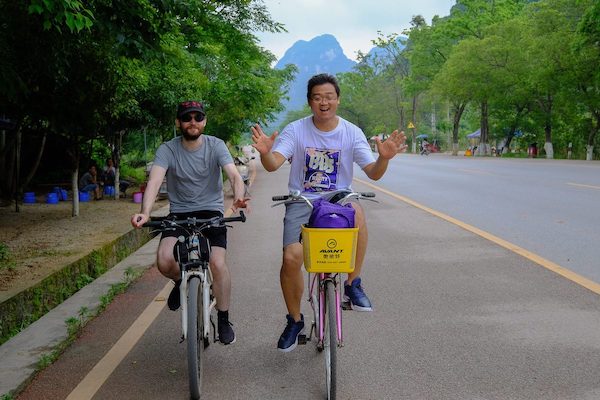 CLI team members ride bikes on a street in Guilin with karst mountains in the background