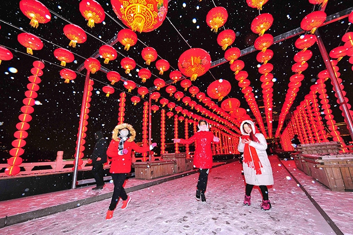 three Chinese women walking under red Chinese lanterns in the snow during celebrations for the Year of the Ox