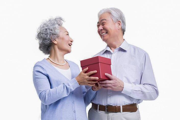 Two Chinese retirees hold a gift box while smiling at each other