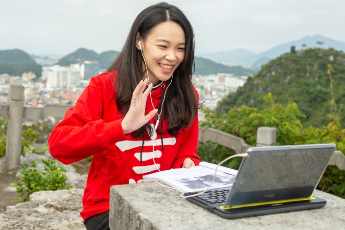 a Chinese teacher waves to her student while teaching online using a laptop