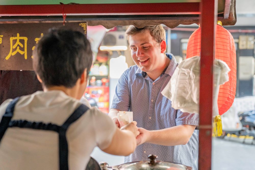 a CLI student using Chinese renminbi to buy a snack from a Guilin street vendor