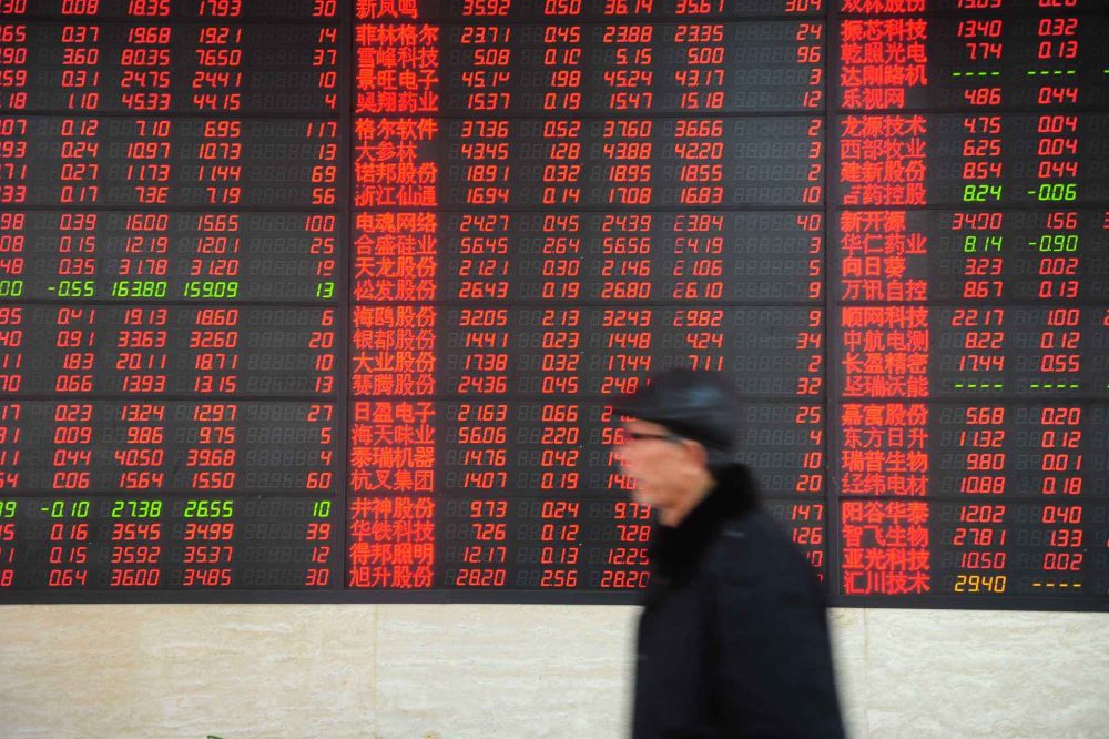 a man walking past a screen showing Chinese stock prices in Chinese renminbi