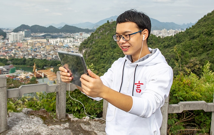 a CLI Chinese teacher talking with a student using a tablet on a mountaintop