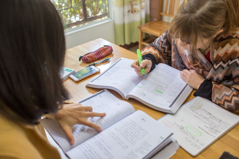a CLI student highlighting text in a Chinese textbook while her Chinese teacher looks on
