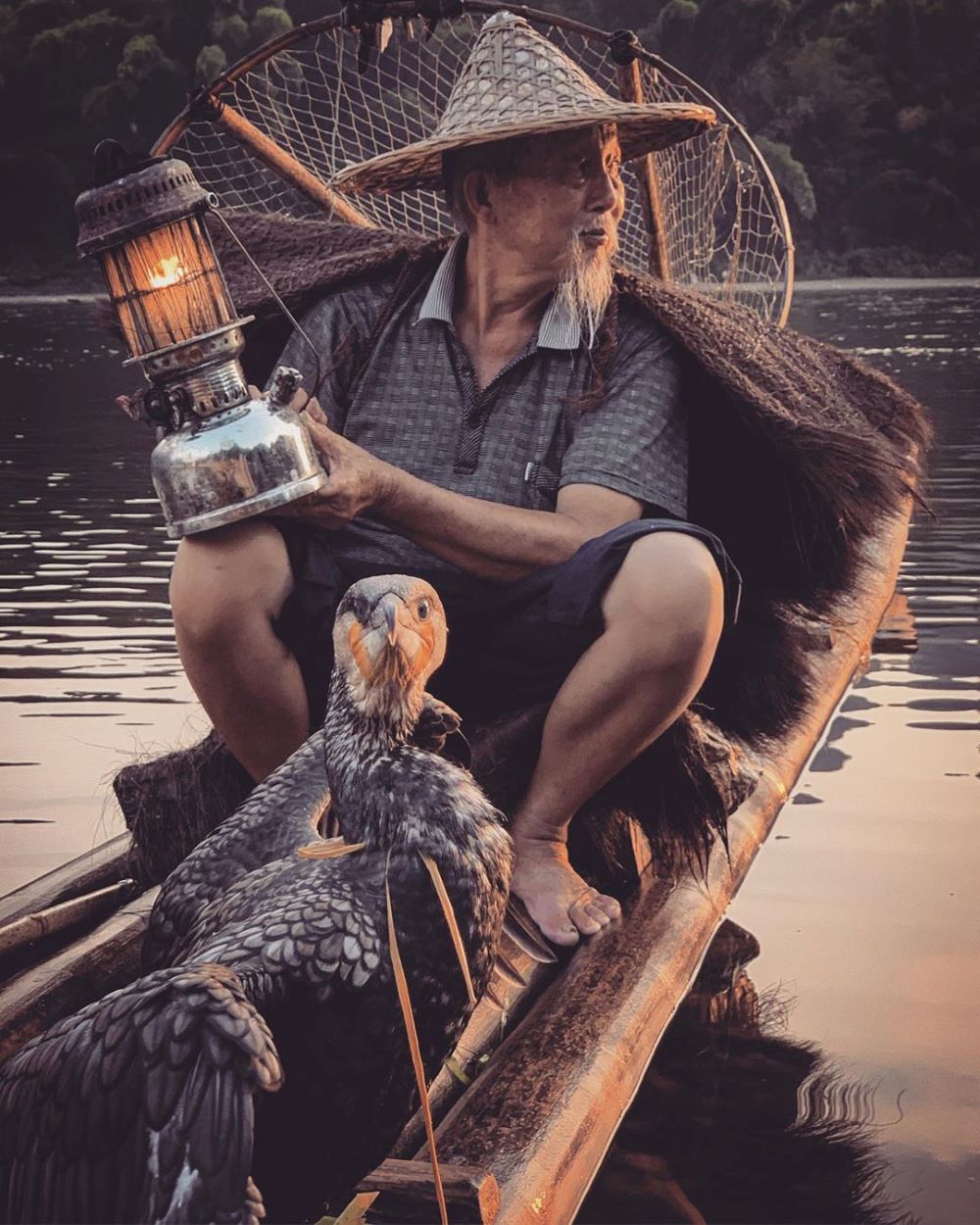 a fisherman with a lantern and a cormorant in a boat on a river outside Yangshuo