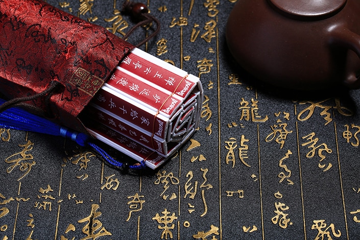 a set of red sticks with white Chinese writing on them in a red silk bag next to a teapot