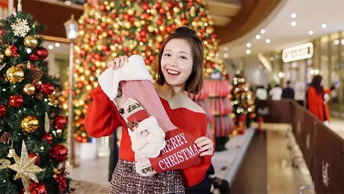 photo of a Chinese woman holding up a Christmas stocking with Christmas trees in the background