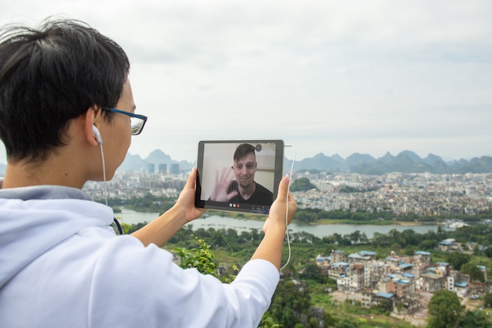 a teacher helping a student learn Chinese on Zoom while standing outside