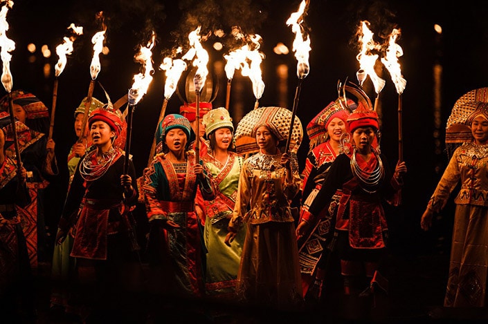 a group of women in Chinese ethnic minority clothes carry torches