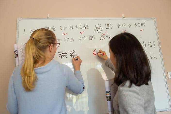 a blond CLI student and her teacher write Chinese characters on a white board