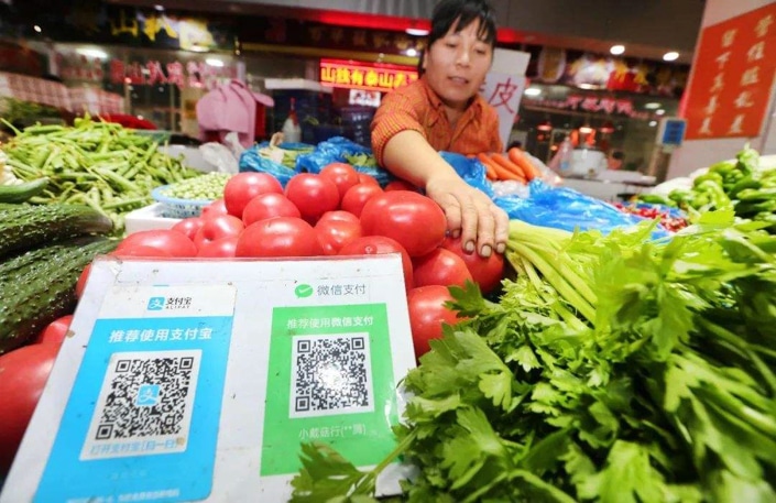 a Chinese street vendor adjusting a bundle of celery with QR codes for WeChat and Alipay in the foreground