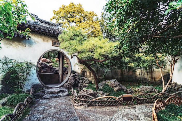 a circular door in a white wall in a traditional Chinese garden, a popular destination for Suzhou travel guides