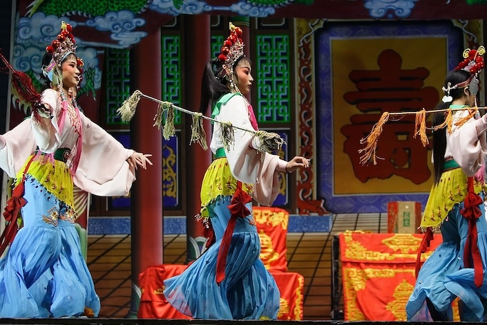 three Chinese opera performers in traditional dress performing a play