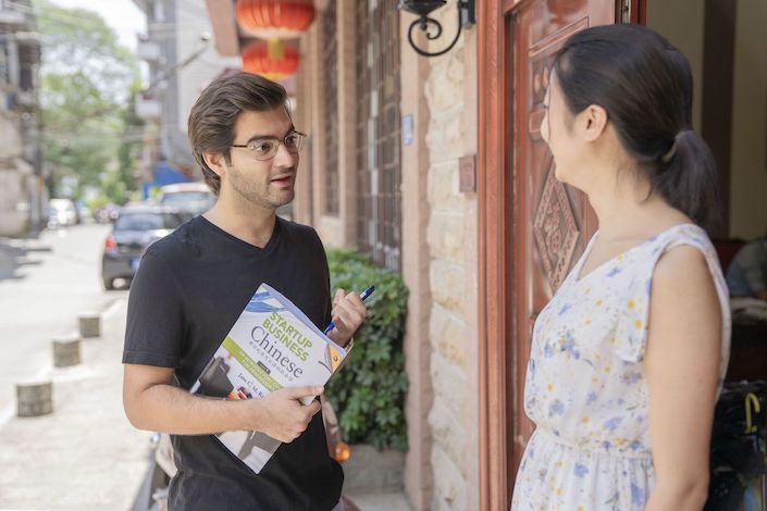 a western man holding a startup business Chinese textbook speaks with a Chinese woman outside the CLI Center in Guilin, China