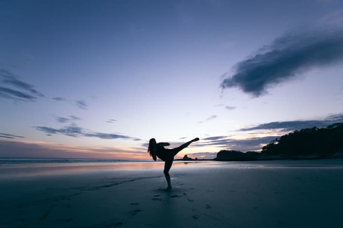 silhouette of a girl doing a kung fu kick on a beach at dusk