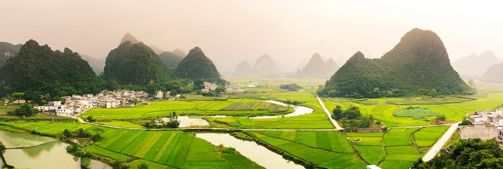 green fields in Guangxi Province, China with karst mountains scattered above them and small streams running through them 