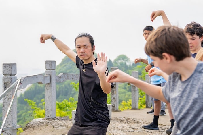 a Chinese man demonstrating a Chinese martial arts move to a group of American students who are trying to imitate him