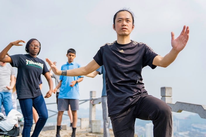 a Chinese martial arts instructor demonstrating a tai chi pose as students look on and copy him