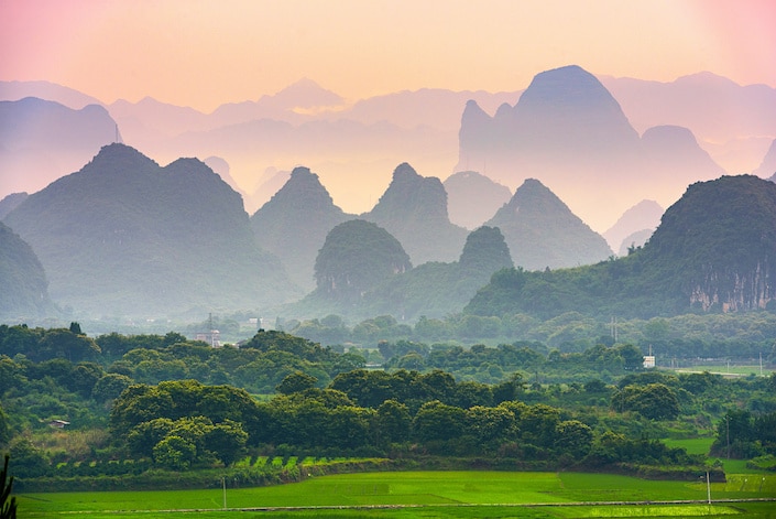 karst mountains rising above a green field and a stand of trees in Guilin, China