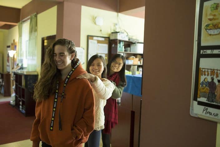 a western woman and two Chinese women standing in single file with their hands on each other's shoulders