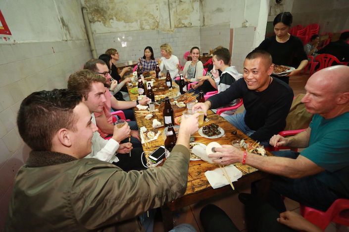 Chinese and western people sitting around a table having dinner in a traditional Chinese restaurant as a server bring more food in the background