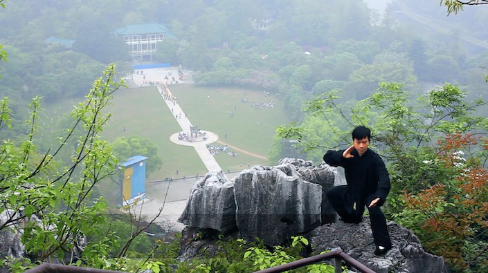 a Chinese man in black practicing tai chi on a mountain