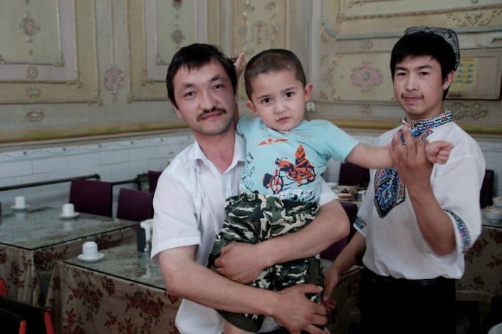 two Uyghur men, one of whom is holding a little boy, inside a restaurant in China
