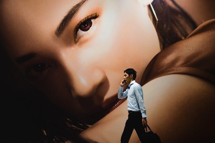 large painting of face in background with young male professional on phone walking in foreground