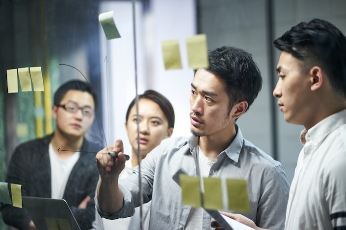 young asian entrepreneur of small company drawing a diagram on glass during team workshop in office discussing and formulating business strategies