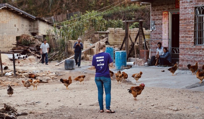 western woman standing in chinese village with back to camera and chickens walking around her