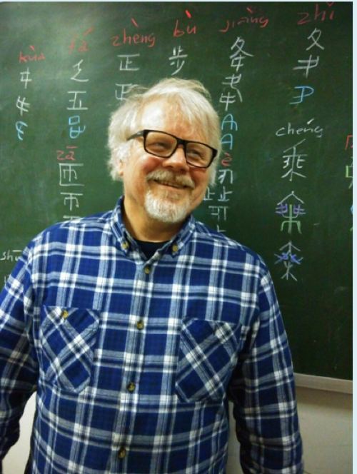 older man with white hair and goatee in front of blackboard with chinese characters