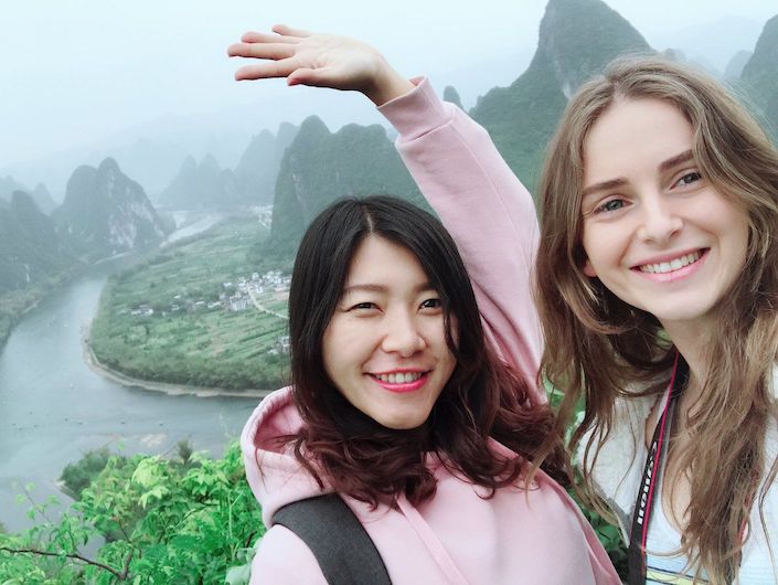 selfie of two young women with big smiles in front of karst mountains and a river