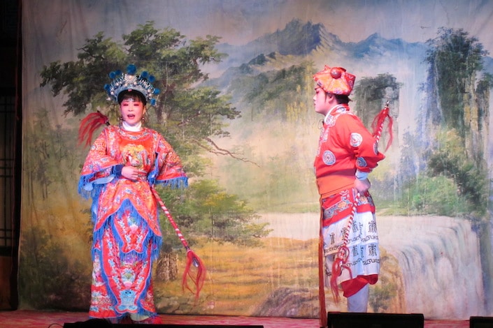two chinese opera performers in front of a landscape oil painting