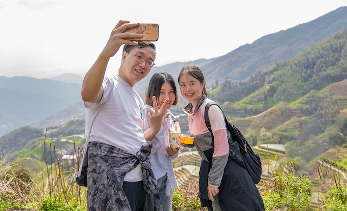 a young chinese man and two chinese young ladies taking a selfie in rice terraces in china