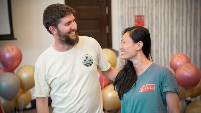 a man with a beard and a chinese woman looking and smiling at each other with balloons in the background