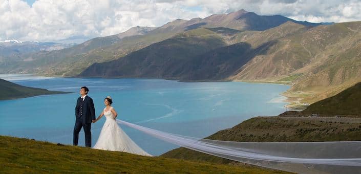 chinese couple in suit and wedding gown with lake and mountains in background