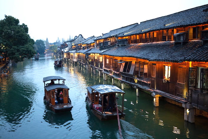 two small wooden boats floating down a canal in wuzhen, china near wooden homes and stores