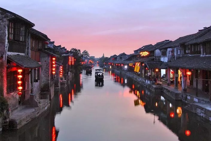 tranquil canal between ancient wooden chinese structures with red lanterns glowing in the water below