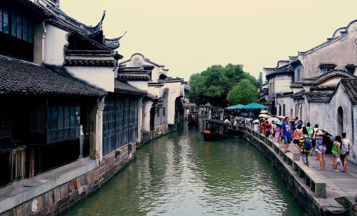 canal in between ancient chinese architecture with tourists walking alongside