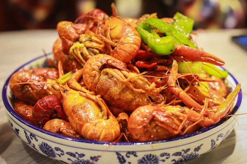 a Chinese blue and white porcelain dish full of cooked crayfish and green bell peppers