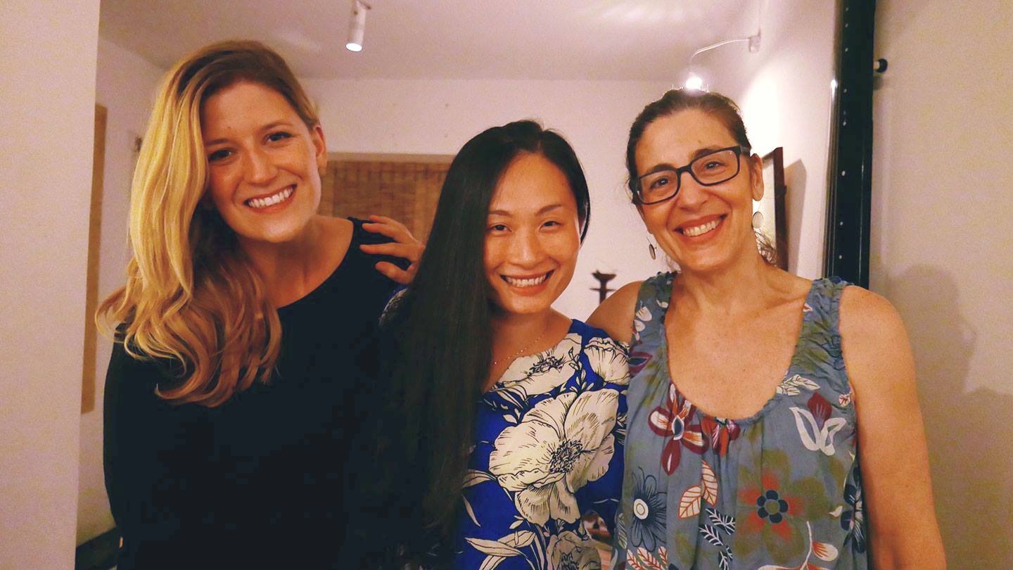 two smiling western women standing on either side of a smiling Chinese women